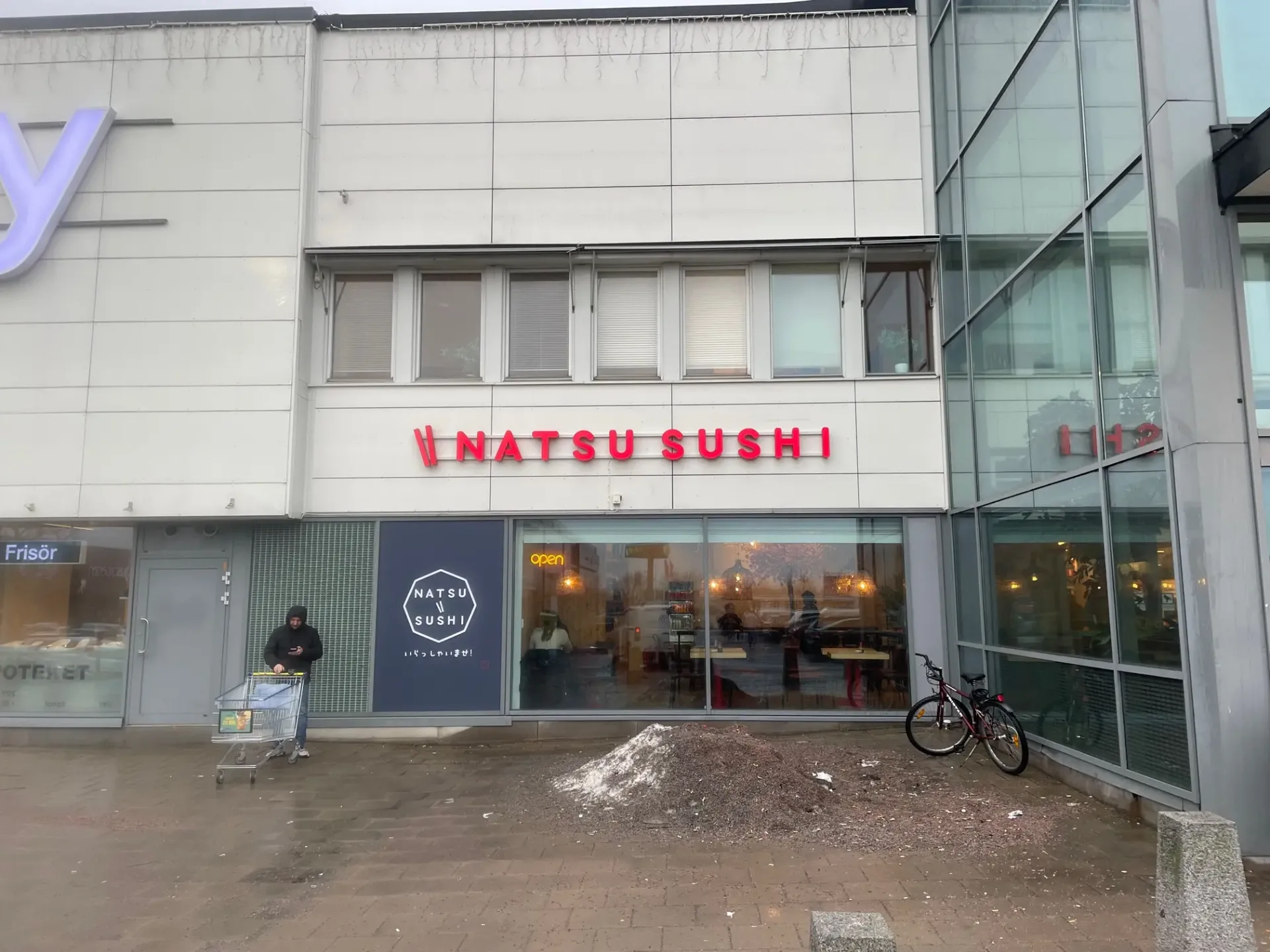 Belyst fasadskylt för Natsu Sushi ovanför restaurangens entré
