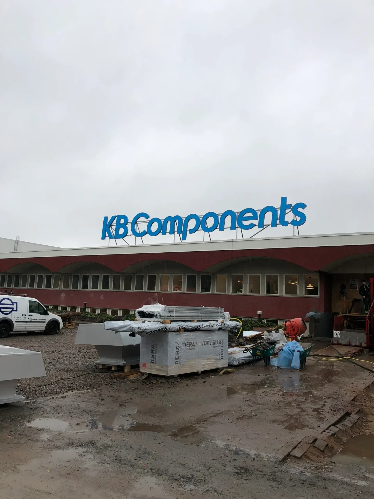 Takskylt med blå profilbokstäver för KB Components på en industribyggnad